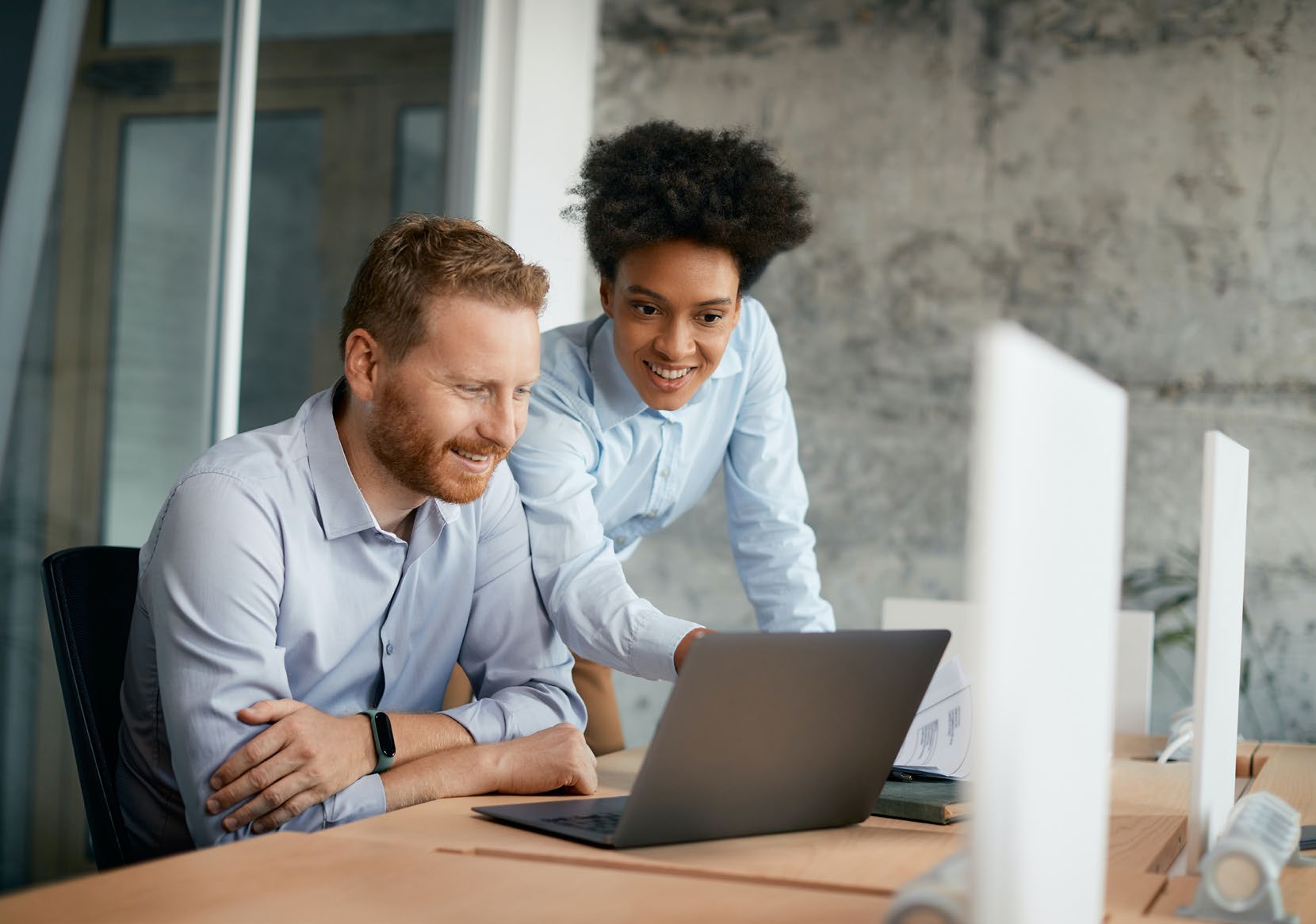 Two colleagues looking together at a laptop screen in an office