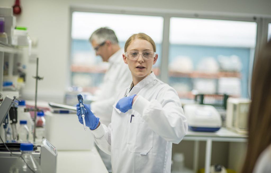 A laboratory scientist holding a pipette in a working lab