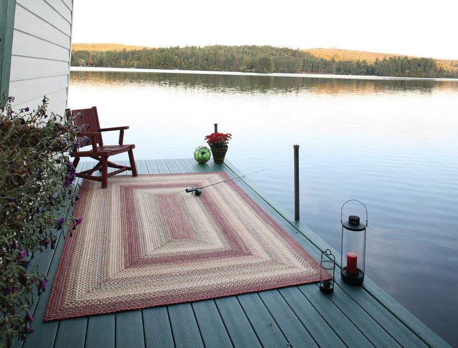 Un tapis tressé posé sur un ponton en bois au bord d’un lac au crépuscule, avec un fauteuil et des lanternes