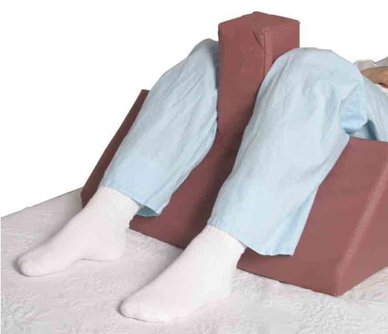 A wedge-shaped leg positioner supporting a patient’s legs on a bed