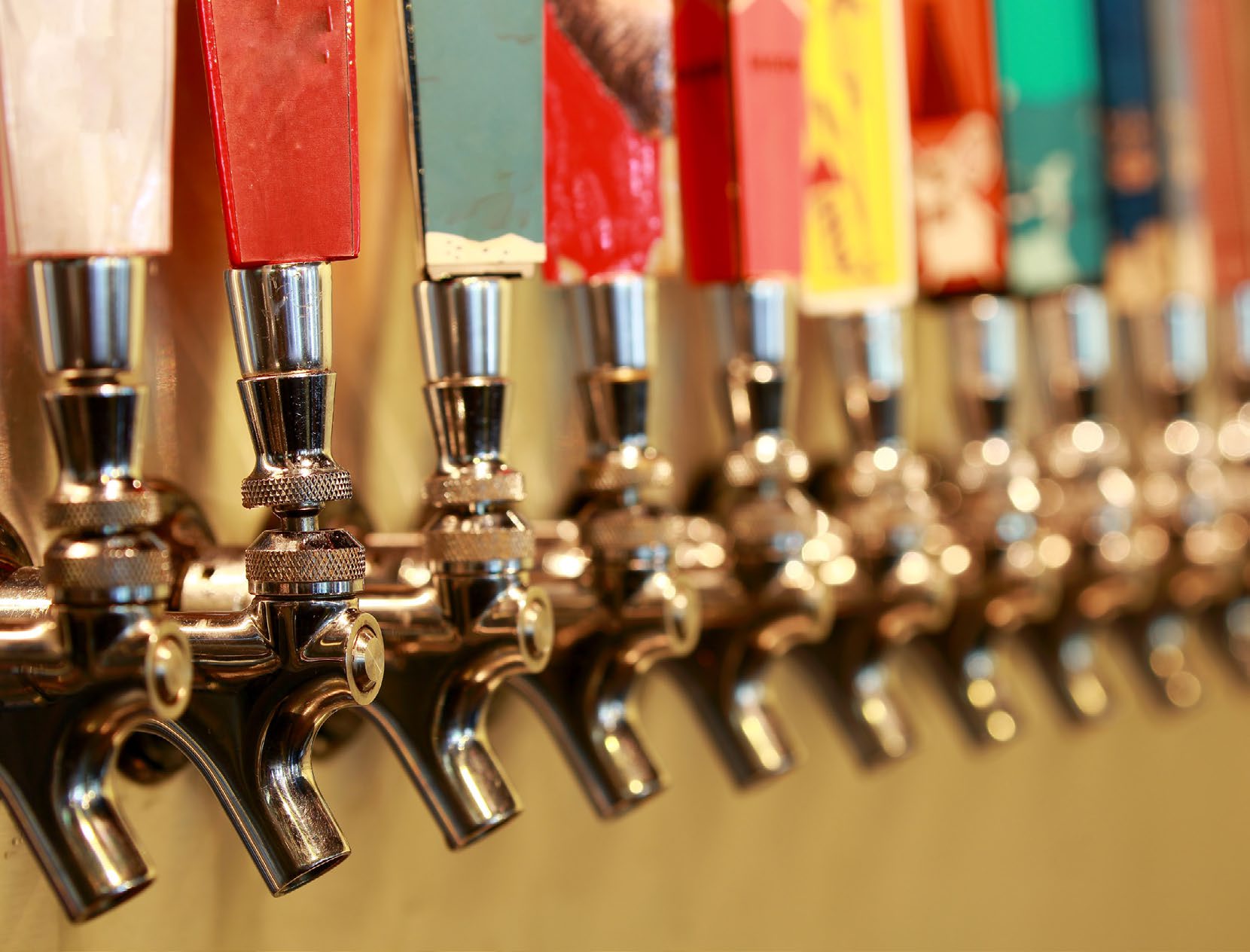 A long row of chrome draught taps with coloured tap handles, receding out of focus