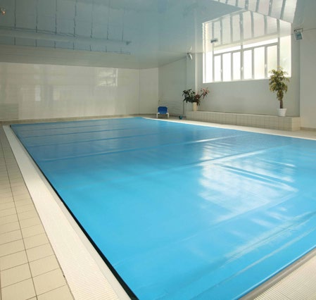 An indoor swimming pool with a blue cover drawn across its full surface