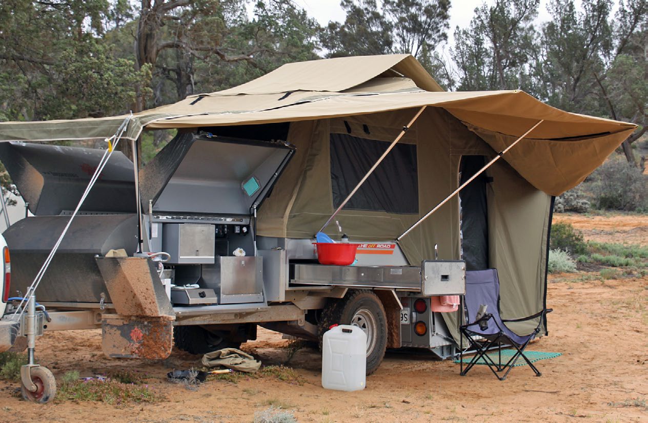 Une remorque de camping Kimberley à plancher rigide, installée, toile déployée et cuisine coulissante ouverte