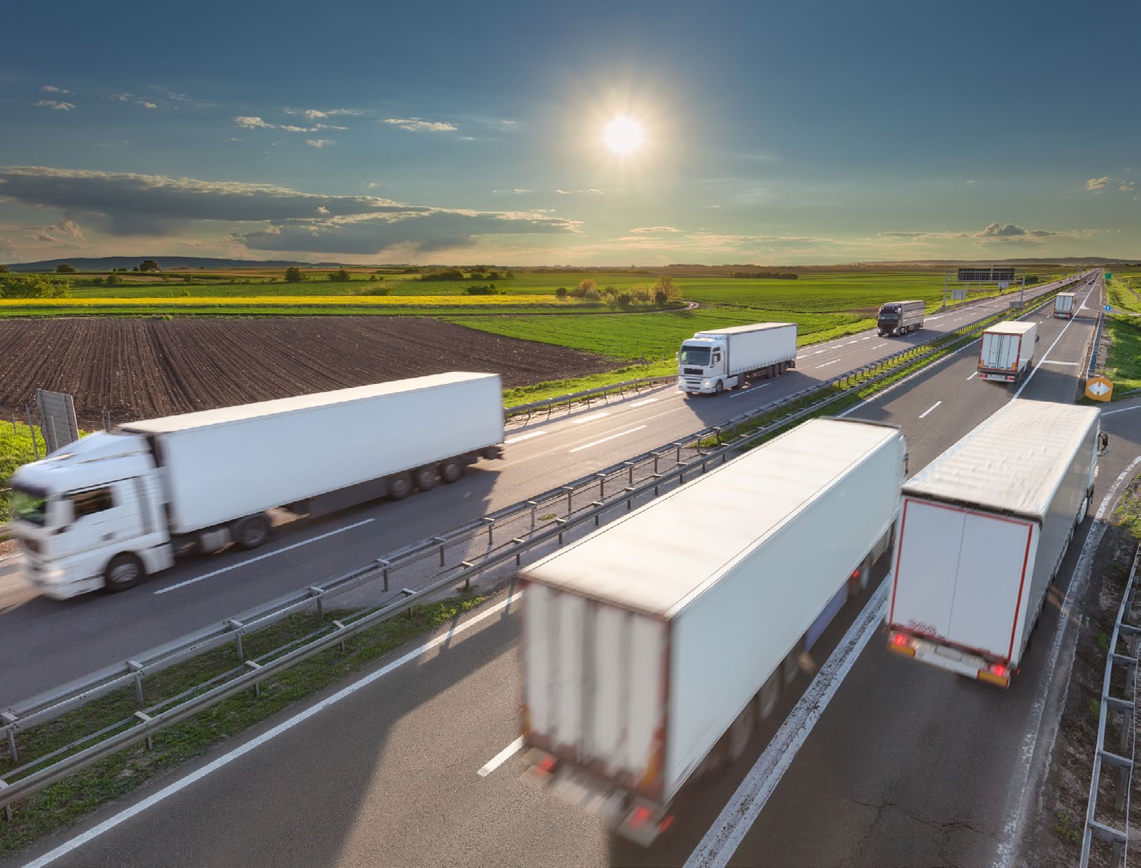 Several articulated lorries on a European motorway at sunset