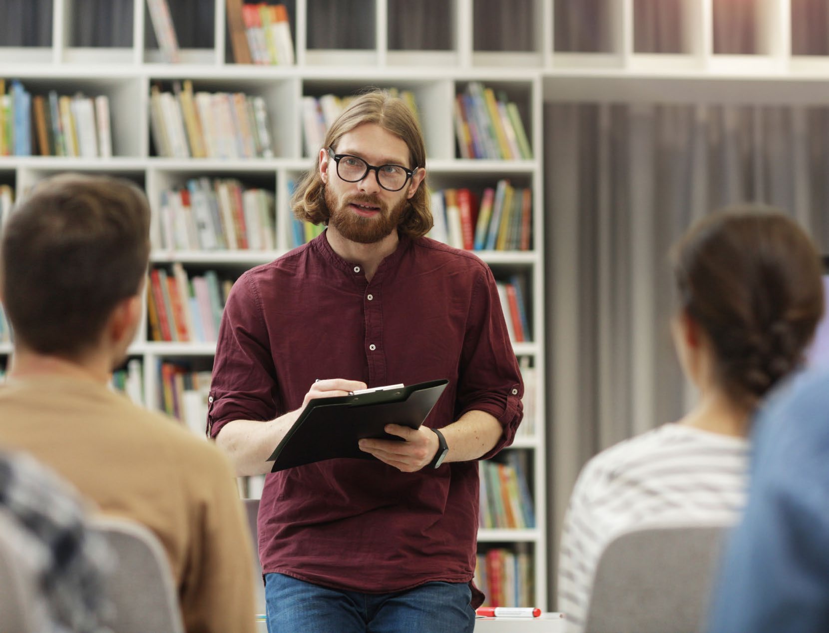 An education professional with a clipboard talking to a small seated group in a school library