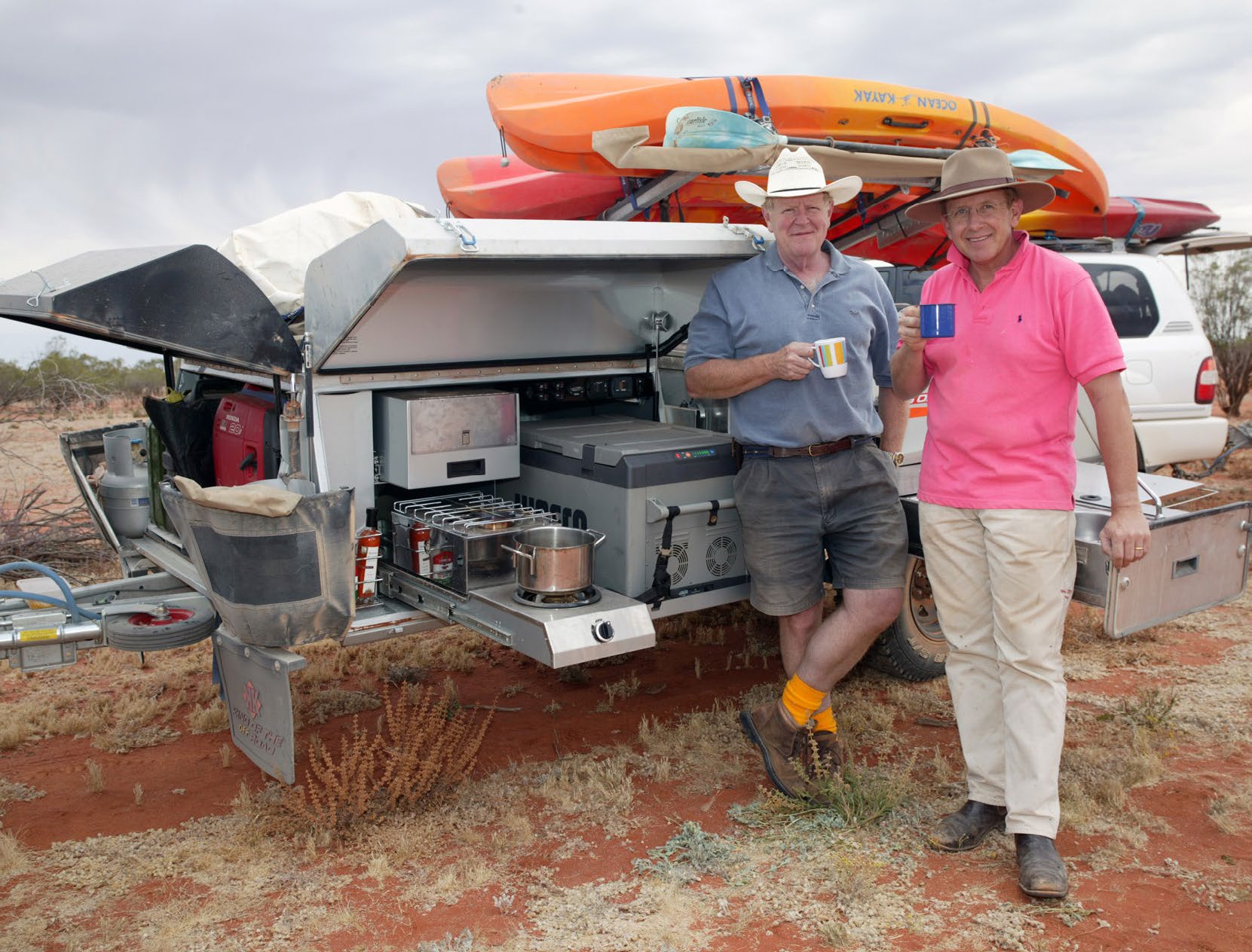 Deux hommes tenant des tasses à côté de la cuisine dépliée d&rsquo;une remorque de camping dans l&rsquo;outback australien