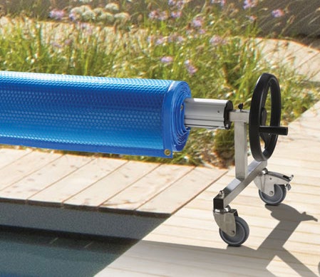 A blue bubble cover wound onto a wheeled roller beside a wooden pool deck