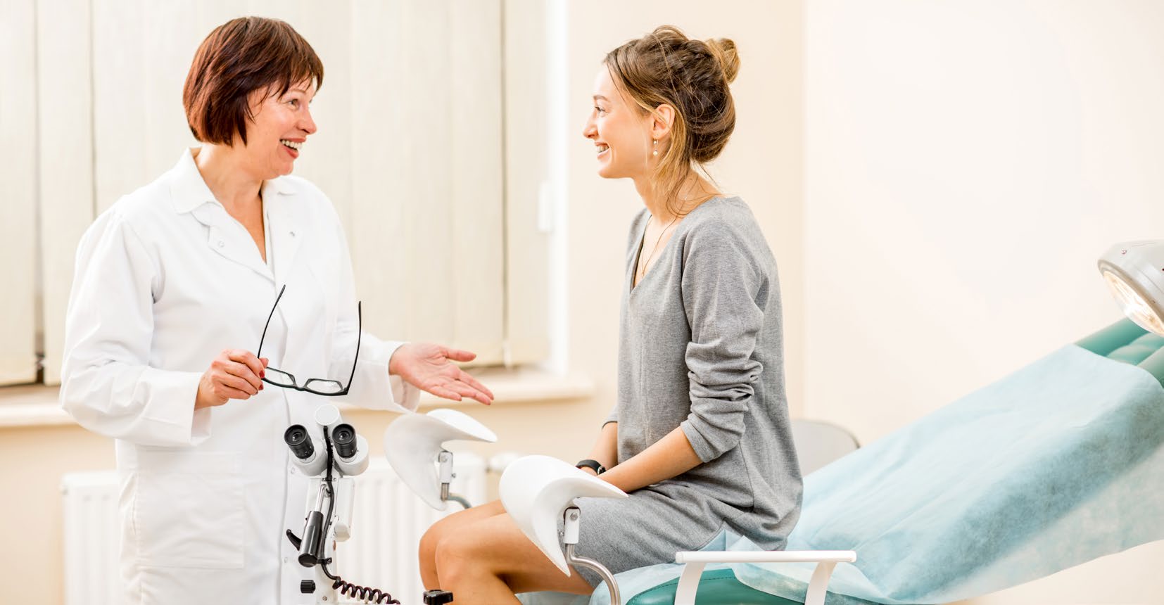 A clinician talking with a patient sitting on an examination couch in a bright clinic room